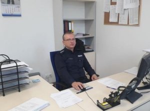 Zdjęcie przedstawia umundurowanego policjanta siedzącego przy biurku.