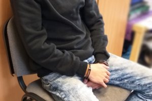 Zdjęcie przedstawia mężczyznę siedzące na krześle z rękoma w kajdankach.